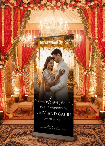 Decorated wedding venue with red and gold drapes, chandeliers, and a couple embracing. A welcome sign for Shiv and Gauri is displayed.
